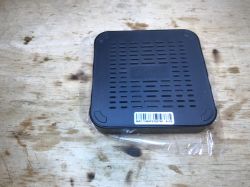 Czarna przystawka TV Box T95MAX leży spodem do góry na drewnianym blacie, widoczny otwór wentylacyjny i naklejka z kodem MAC.