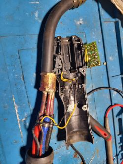 Zdjęcie rozkręconego palnika z widocznymi przewodami i obudową na niebieskim tle.