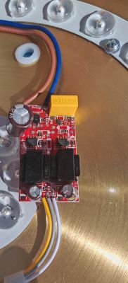 Płytka sterownika LED na czerwonym PCB z przewodami i elementami, obok moduł LED z soczewkami