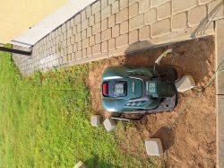 Robot koszący Parkside znajduje się w swojej bazie przy krawężniku, otoczony kilkoma betonowymi bloczkami i przewodami.