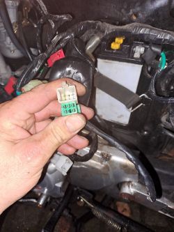 Ręka trzyma złącze elektryczne przy motocyklu Romet Ogar 202 podczas wymiany silnika.