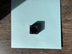 Czarny plastikowy element o kwadratowym przekroju z okrągłym otworem, na jasnym tle