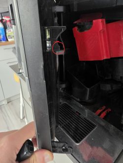 Zbliżenie na wnętrze drzwiczek ekspresu; czerwonym kółkiem zaznaczony ułamany plastikowy zaczep.