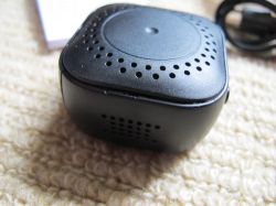 Portable Speaker on Carpet A small, black, square portable speaker is lying on a light carpet.