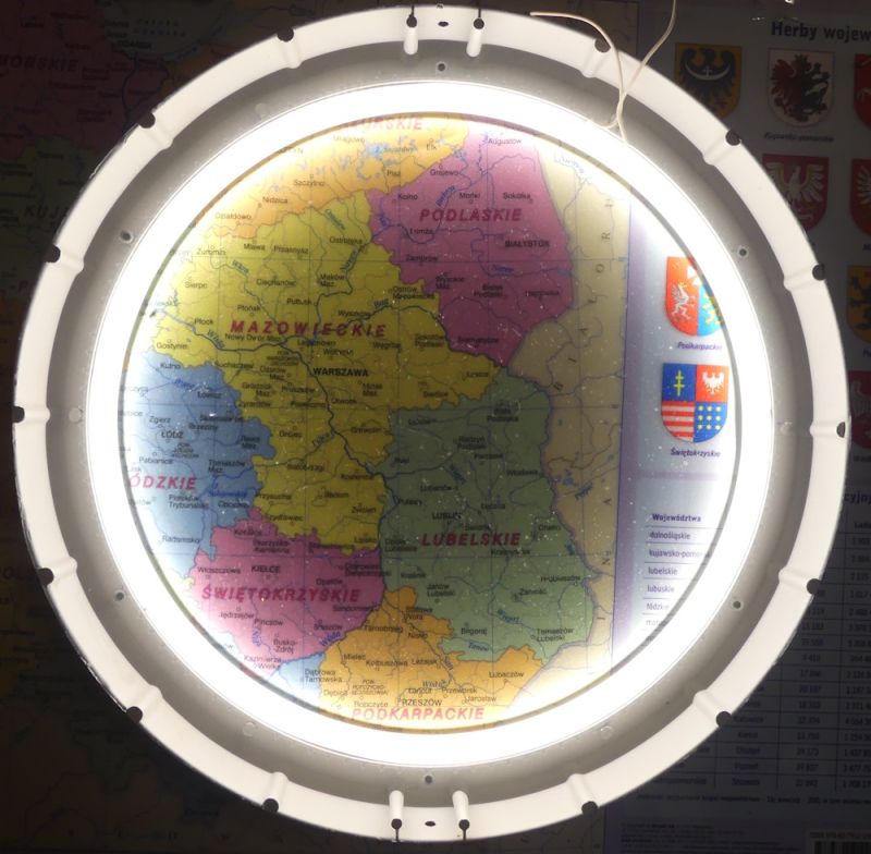 Podświetlona lupa nad mapą Polski z widocznymi województwami i herbami po prawej