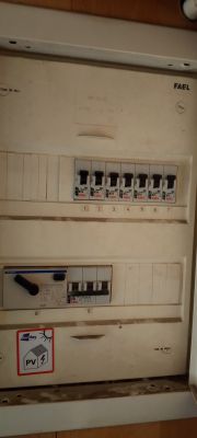 Panel elektryczny z kilkoma bezpiecznikami FAEL oraz głównym wyłącznikiem nadprądowym i naklejką z symbolem fotowoltaiki.