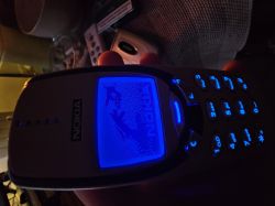Nokia 3310 phone with a blue backlit screen in a dark setting.