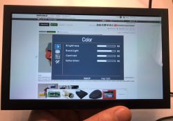 LCD screen showing image settings menu, held by hand in front of a website