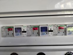 Panel z licznikami energii i ogranicznikami napięcia marki Schneider Electric, pokazujący wartości napięcia około 247-248V.
