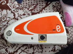 Bateria rowerowa BionX KTM Electric Series z gniazdem ładowania i kluczykiem, leżąca na dywanie.