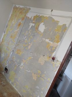 Zniszczona ściana z widocznymi kablami elektrycznymi i puszkami.