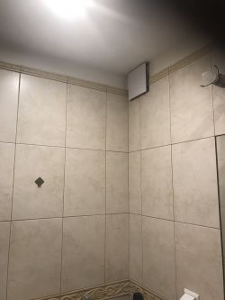 Wentylator zamontowany w rogu łazienki na ścianie z płytkami.