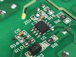 Zbliżenie na płytkę drukowaną z elementami elektronicznymi SMD, widoczny układ scalony oznaczony jako U1 oraz kilka rezystorów i kondensator.
