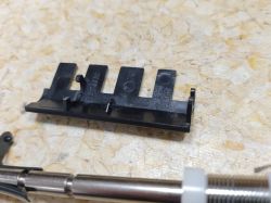 Plastikowy element o nazwie grzebień do drukarek Lexmark obok metalowego pręta.