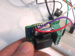 ATLO-SW1-TUYA during firmware update soldering ATLO-SW1-TUYA relay module with soldered wires for programming, close-up view of the circuit board and electronics.
