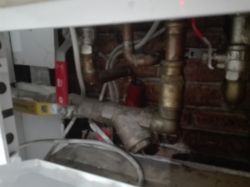 Zdjęcie części instalacji hydraulicznej z przewodami i rurami wokół pieca centralnego ogrzewania.