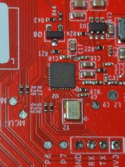 Close-up of a red printed circuit board with electronic components such as an integrated circuit and a crystal oscillator.