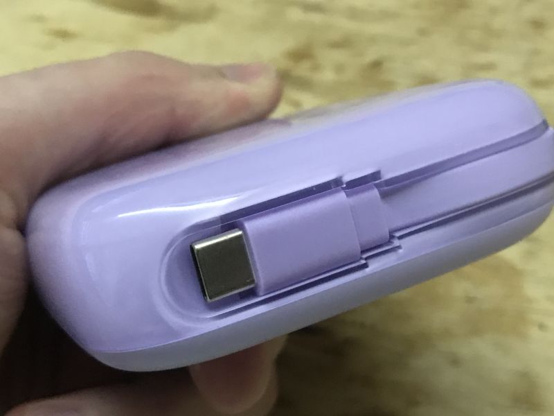 Zbliżenie na port USB-C w wbudowanym kablu w fioletowym powerbanku.