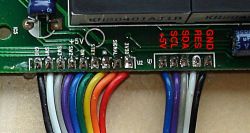 Close-up of ribbon cable connected to PCB with labeled signal and power pins