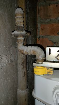Zawór gazowy w instalacji mieszkaniowej z żółtą etykietą na mierniku.