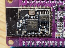 Electronic module on a purple PCB with visible components and chips.