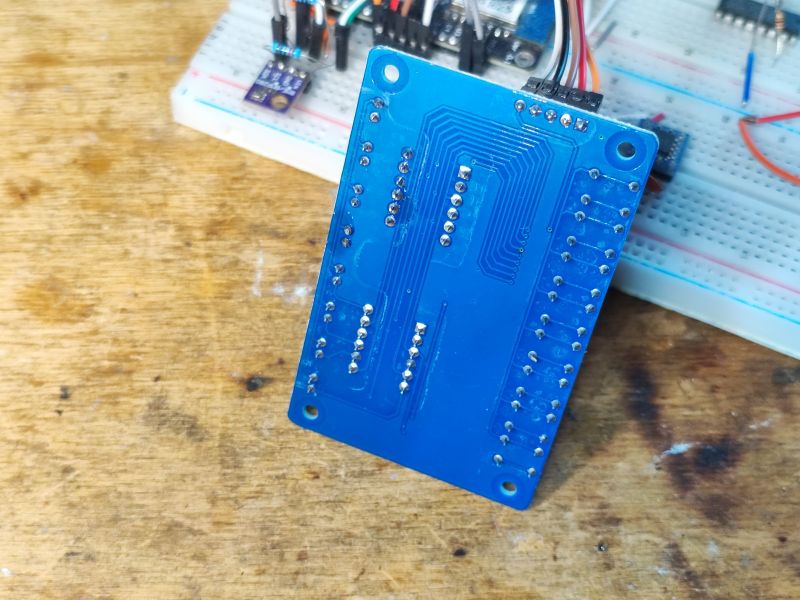 Tył niebieskiej płytki PCB z widocznymi ścieżkami i otworami montażowymi.