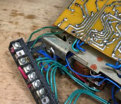 Close-up of device internals with PCB, screw terminal block, and bundled wires on a wooden surface