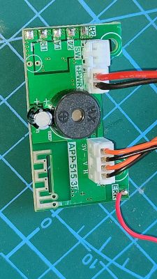 Zielona płytka PCB z dwoma białymi złączami, brzęczykiem i ścieżką antenową na macie do cięcia