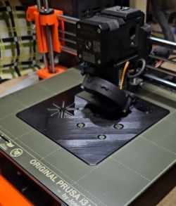 Drukarka 3D Original Prusa i3 MK3 drukująca czarną płytę czołową metronomu.