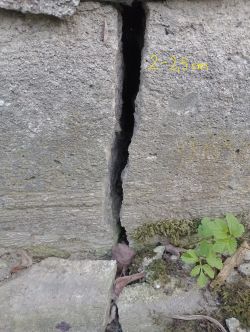 Pęknięcie w murze betonowym z miarką wskazującą szerokość 2-2,5 cm.