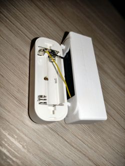 WiFi Thermometer with Additional Battery Housing Open case of a white thermometer with two springs and a yellow wire inside, next to an additional battery housing.