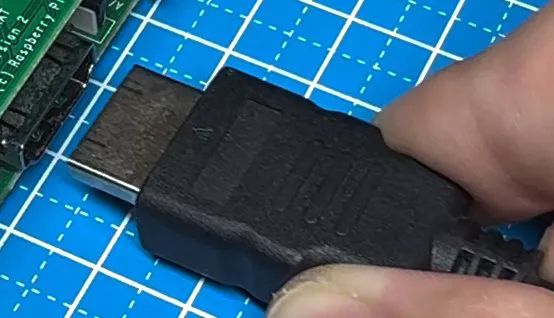 Osoba trzyma złącze HDMI przed podłączeniem do płytki elektronicznej na niebieskiej macie technicznej.