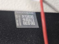 Naklejka z kodem QR i numerami na czarnej, chropowatej powierzchni; po prawej czerwony przewód