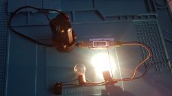 Akumulator narzędziowy, tester USB z wyświetlaczem i żarówka jako obciążenie na niebieskiej macie