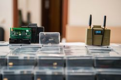 Electronic devices on a table, including a green circuit board and a device with antennas.