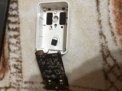 Disassembled device: white plastic case and black PCB with a USB port on patterned fabric