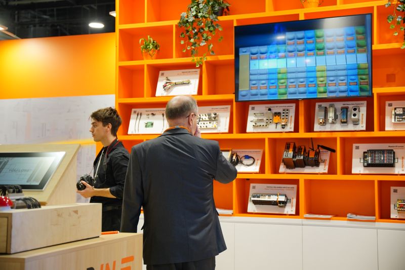 Two men at a trade booth with industrial electronics and a touch screen