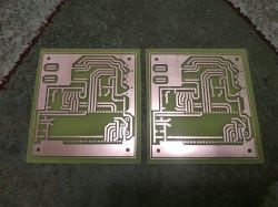 Two green PCBs with copper traces placed side by side on a patterned carpet