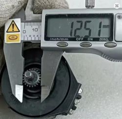 Cyfrowy suwmiarka mierzy średnicę małej metalowej zębatki, wskazując wartość 12,51 mm.