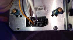 Zbliżenie na złącze elektryczne z przewodami oraz metalową obudową, widoczny kod kreskowy z numerem seryjnym.
