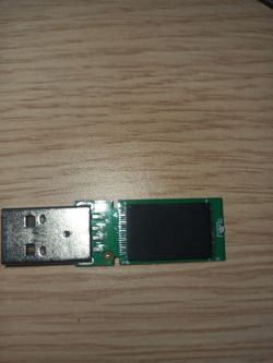 The image shows a disassembled USB key with visible internal circuits on a wooden surface.
