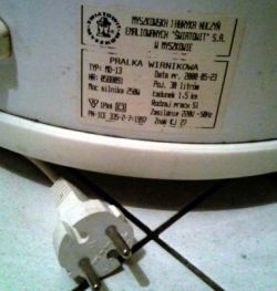 Tabliczka znamionowa pralki wirnikowej z wtyczką elektryczną na podłodze.