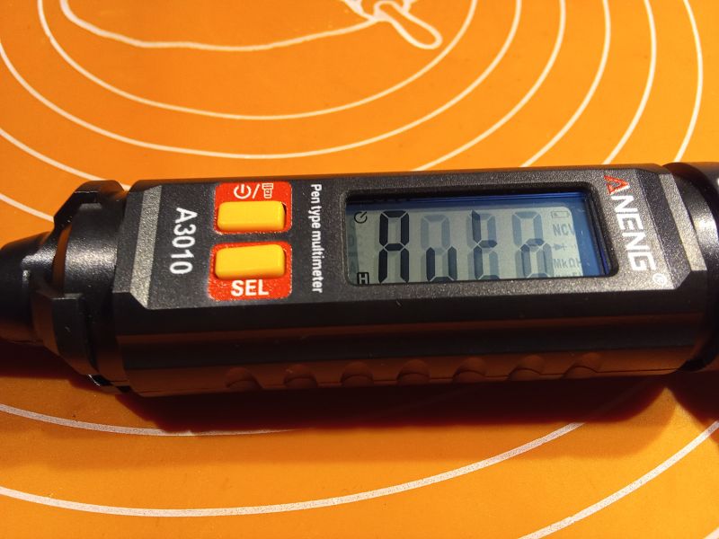 Multimetr w kształcie wkrętaka firmy ANENG na tle pomarańczowym.