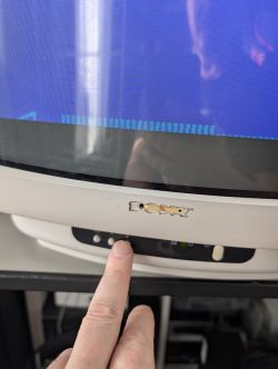 Palec naciska przycisk na przednim panelu telewizora Sony Trinitron z widocznym niebieskim ekranem.