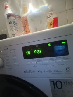 Panel pralki z wyświetlaczem elektronicznym i butelkami detergentów na górze.