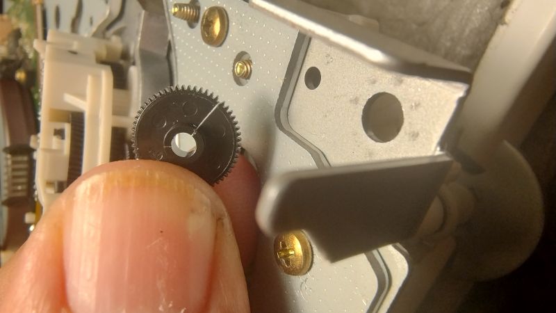 Zbliżenie na małą czarną zębatkę trzymaną palcami przy mechanizmie magnetowidu