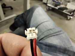 Zbliżenie na białą wtyczkę z dwoma przewodami, czerwonym i czarnym, trzymaną w dłoni.