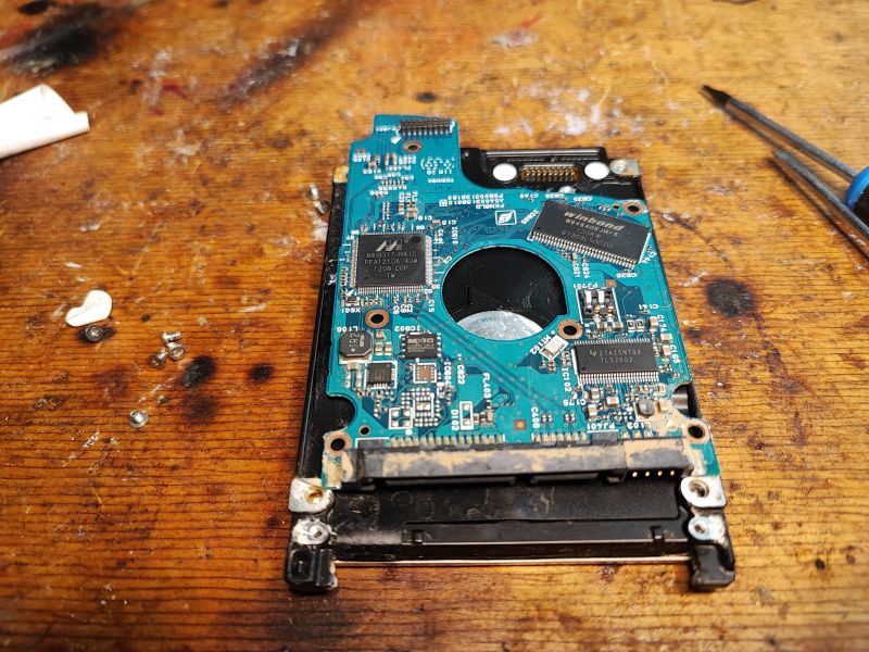 Hard Drive Interior on Wooden Surface Image of a hard drive interior with a visible PCB on a wooden surface.