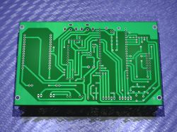 Bottom side of a green PCB with visible traces and through-holes on a blue background