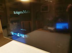 Telewizor Kruger & Matz z włączonym ekranem startowym, częściowo podświetlonym.
